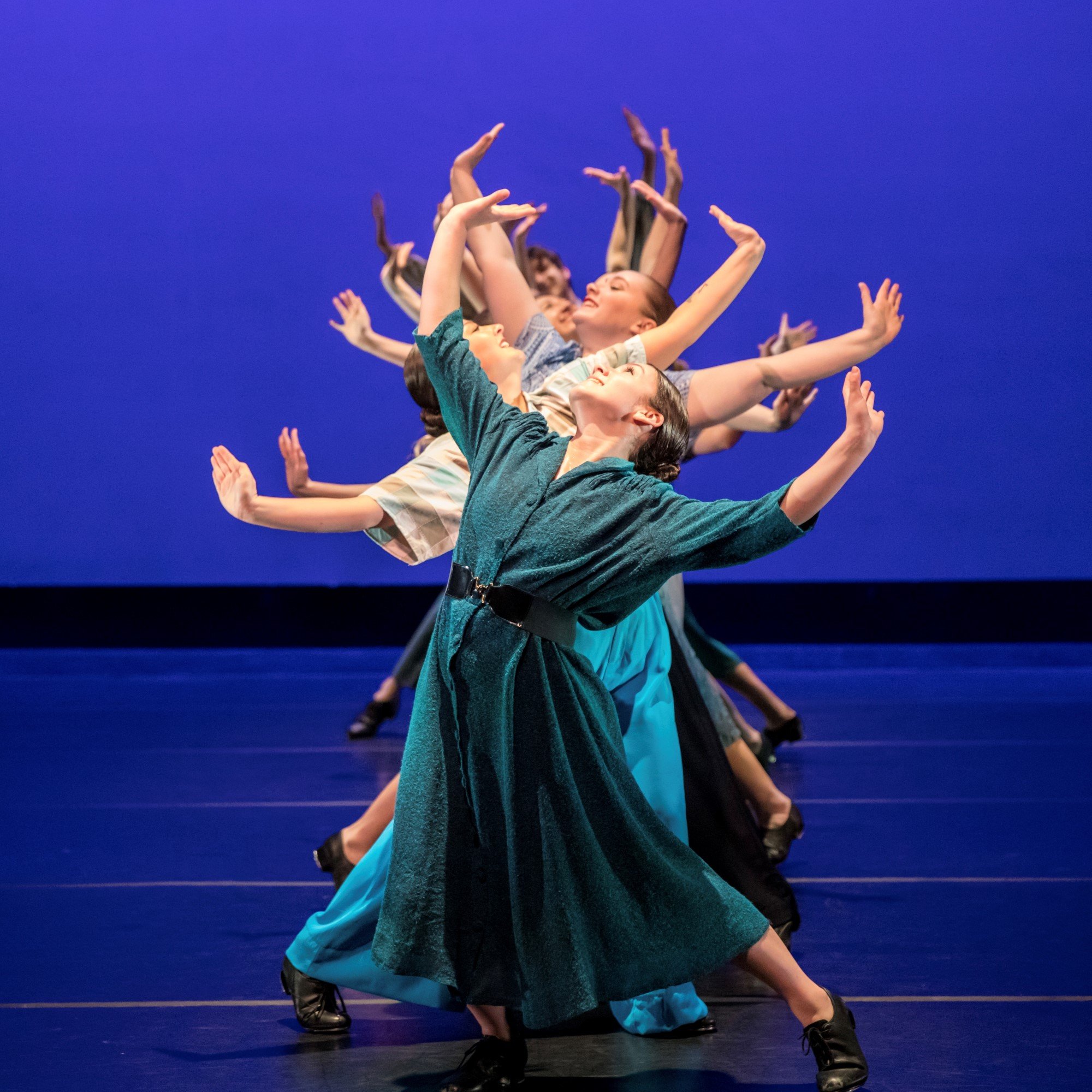 line of tap dancers with their arms raised over head