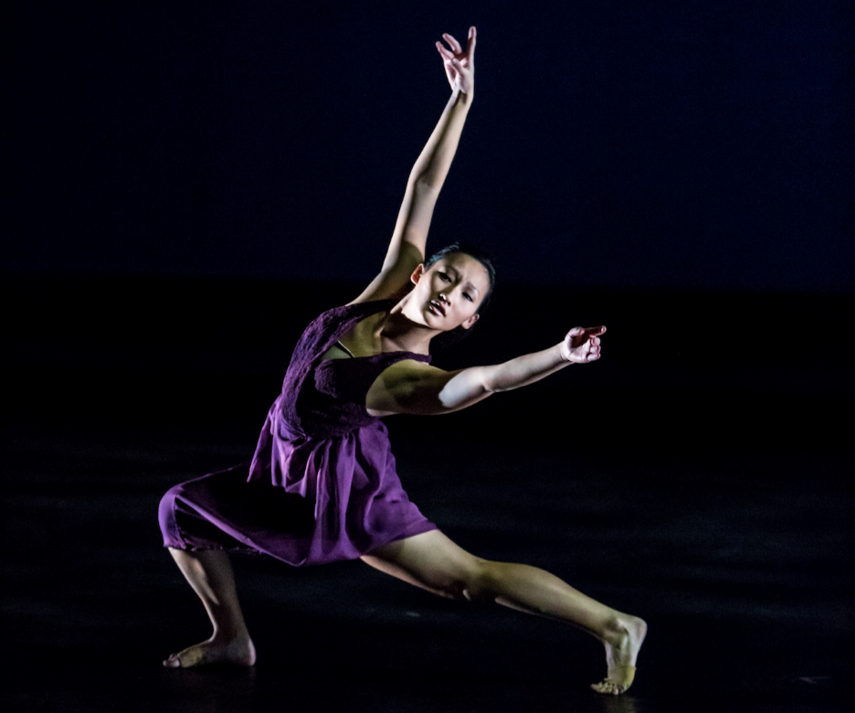 A women dancing on a dark stage with a subtle spot light on her