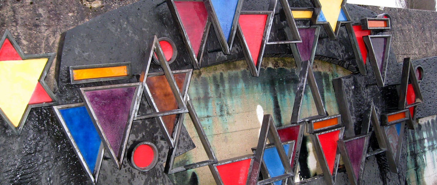  Star, round, triangle, and rectangle shaped steel structures with red, yellow, blue, green, purple, and dark orange colors painted insides hung in a wall