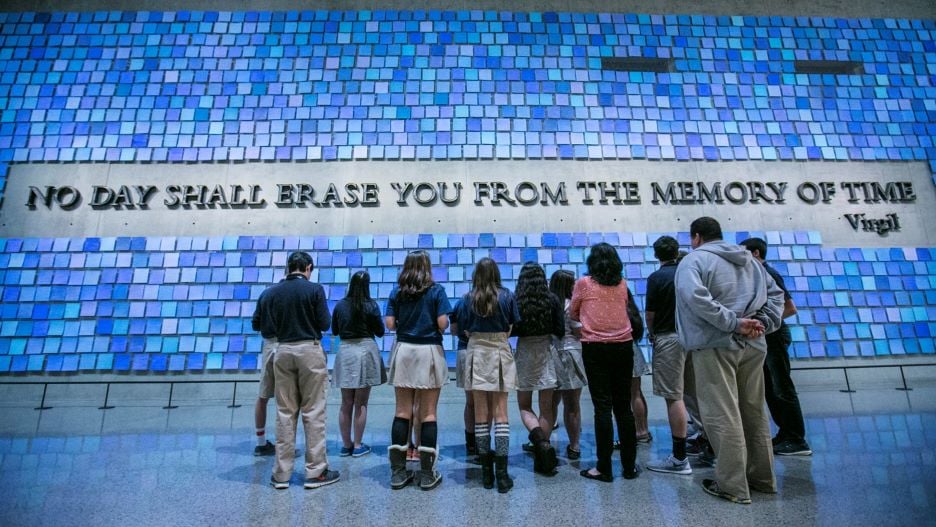 Students and teacher standing in front of a memorial that says "no day shall erase you from the day of time" by Virgil