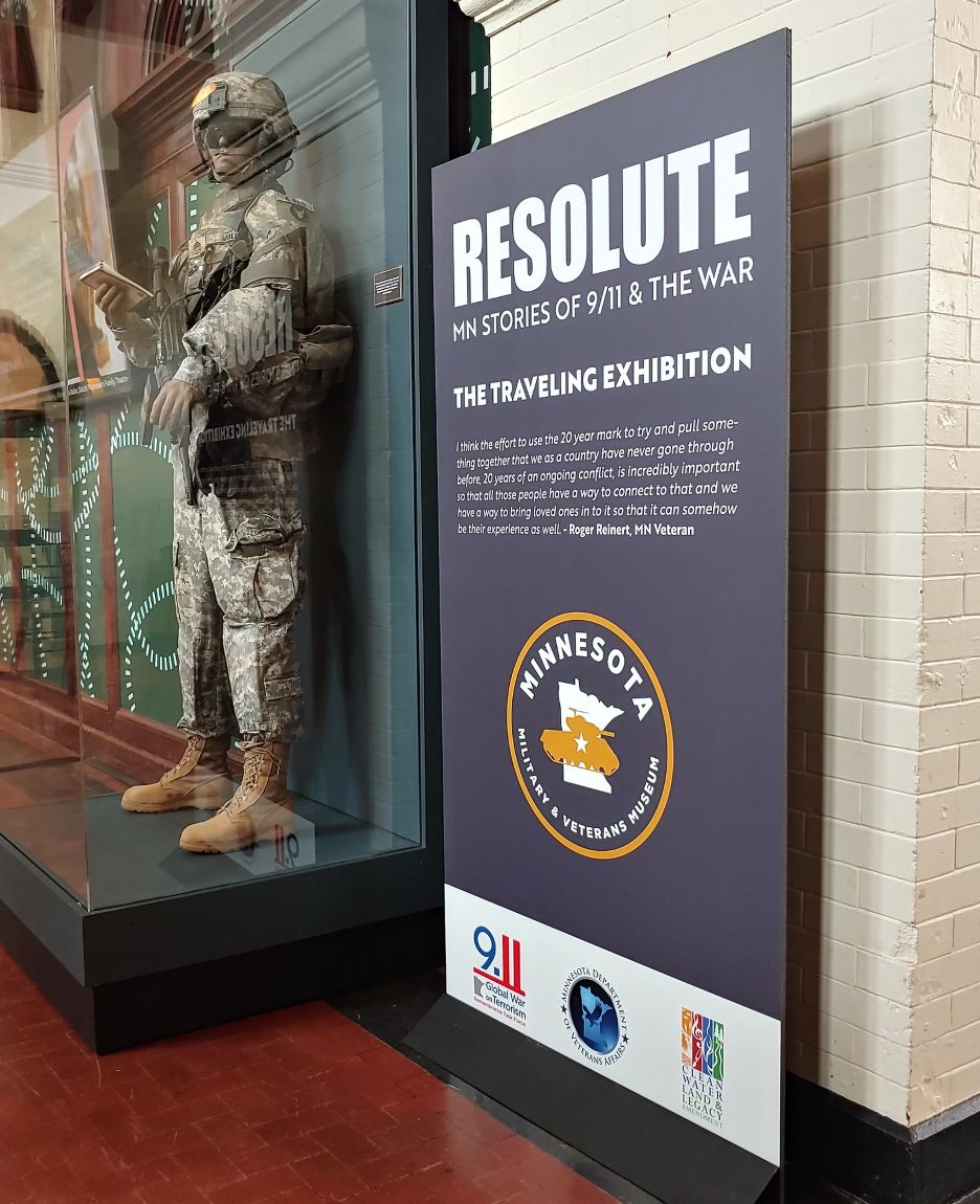 Closeup of the Resolute: MN Stories of 9/11 and The War Traveling Exhibit poster and uniform in a glass case