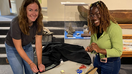 Two Minnesota State Mankato Department of Art and Design students posing while sowing fabric for an exhibit at the Blue Earth County Historical Society museum