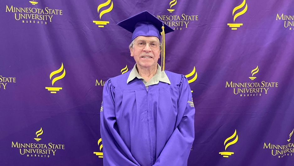 Graduate in cap and gown in front of purple university background
