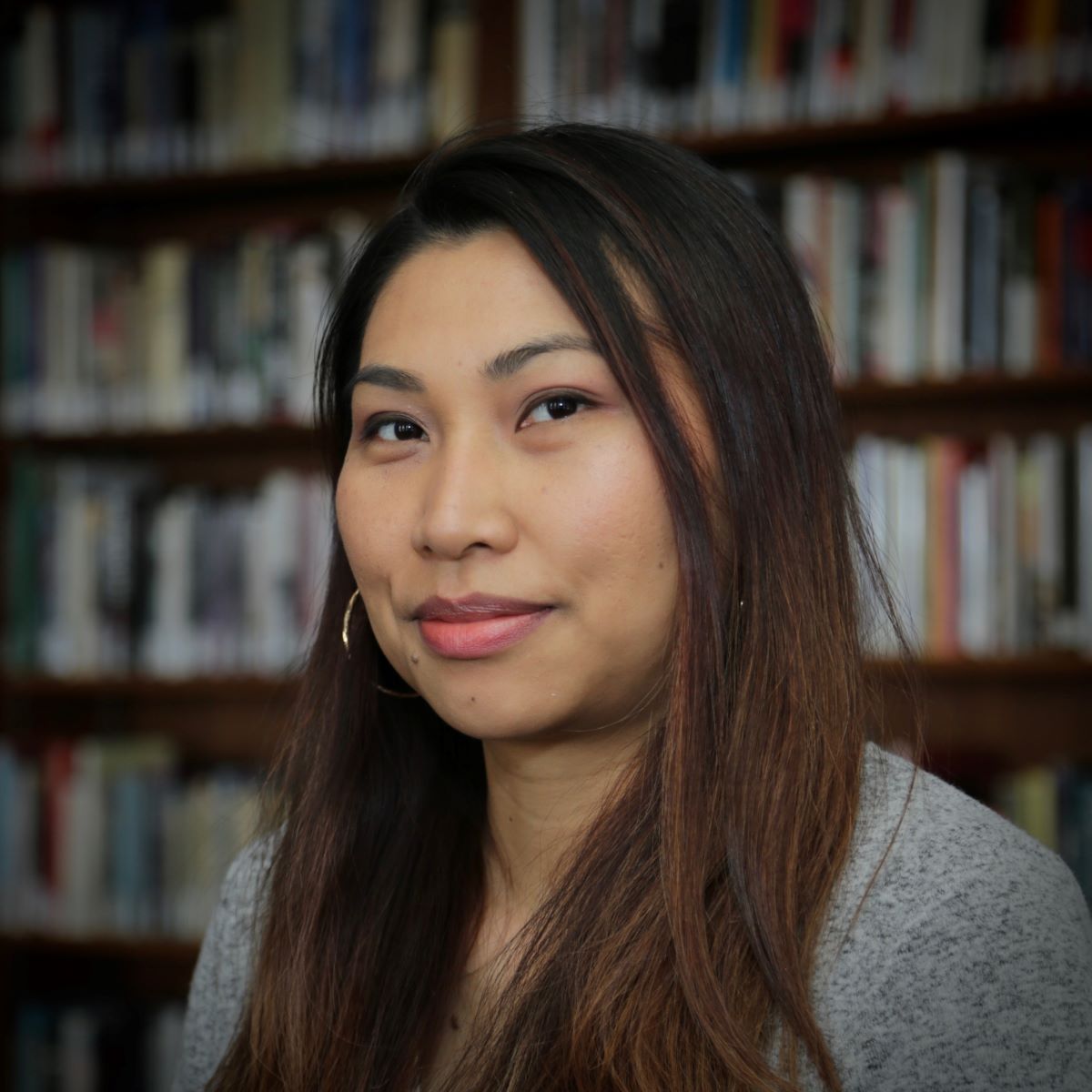 a person smiling in front of a bookshelf