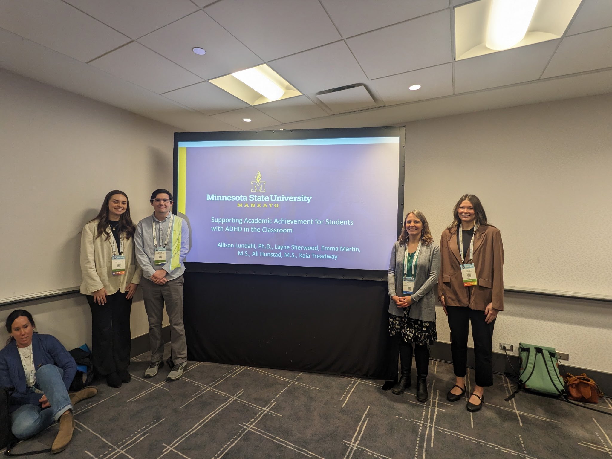A group of five presenters stand in front of a projection screen displaying a Minnesota State University, Mankato presentation titled &lsquo;Supporting Academic Achievement for Students with ADHD in the Classroom.&rsquo;