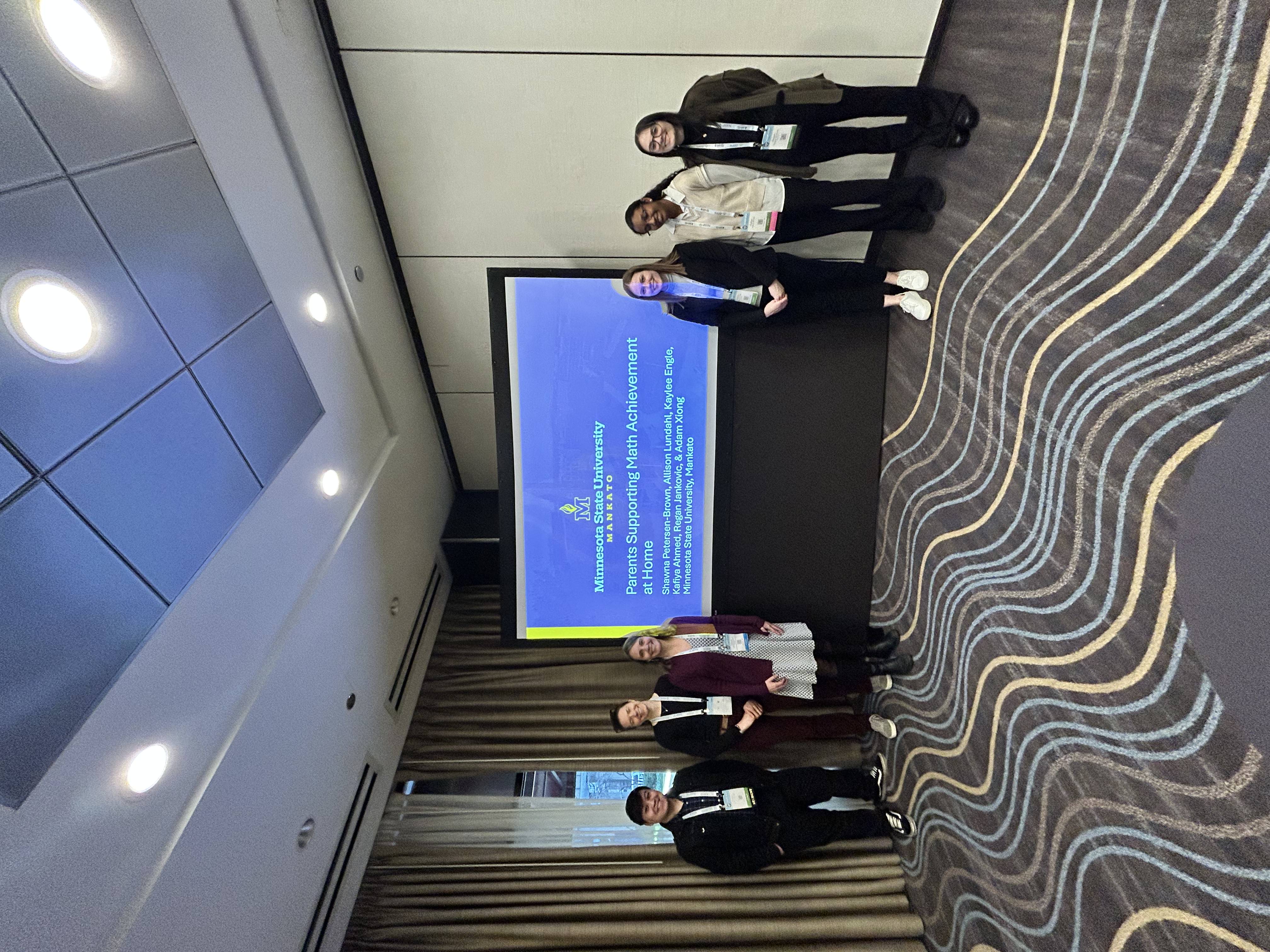 Attendees gather and interact in a conference space during a presentation or poster session.