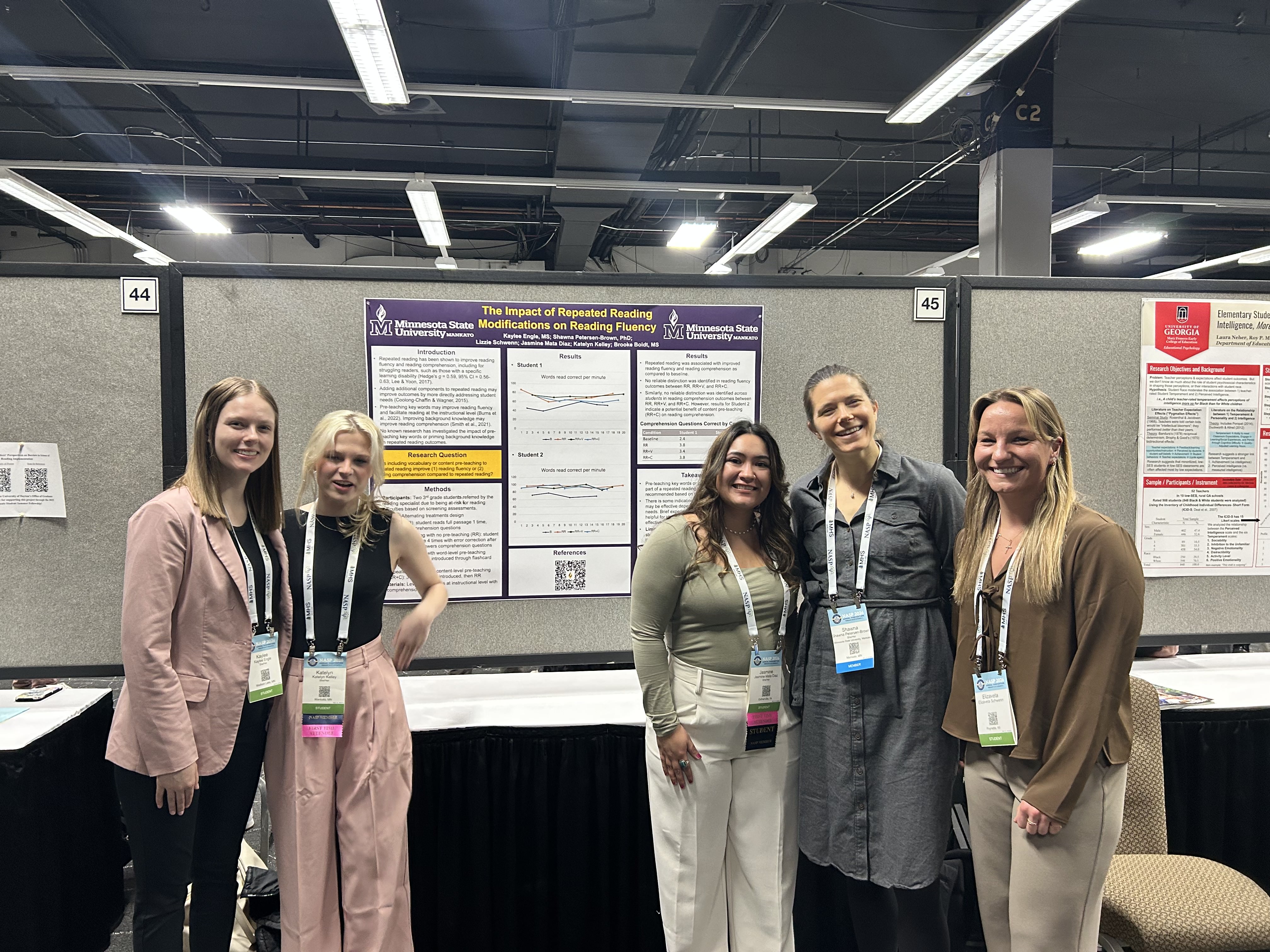 Group of five atendees taking a picture infront of their presentation poster