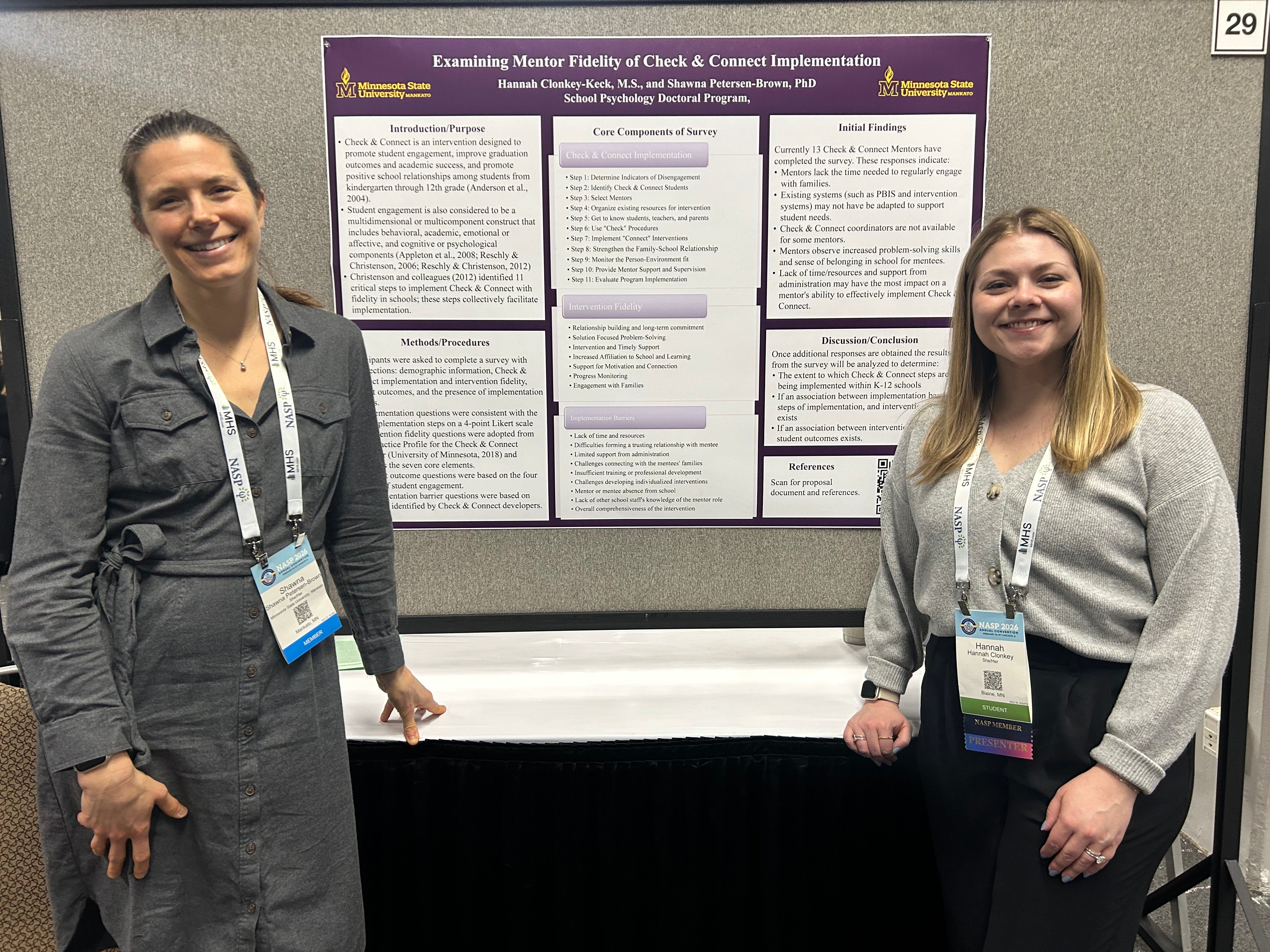 Two presenters stand beside a research poster from Minnesota State University, Mankato, smiling at a conference