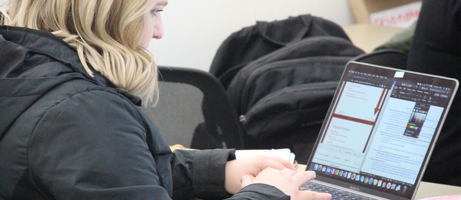 A student sitting at a table in a study area typing on a laptop