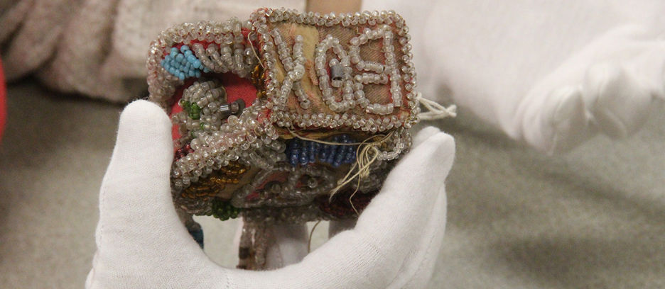 A cloth box decorated with beads held by someone wearing a white cloth glove