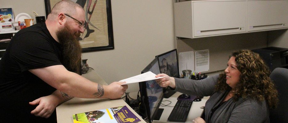 A male student collecting a paper from the administrative staff at the front desk