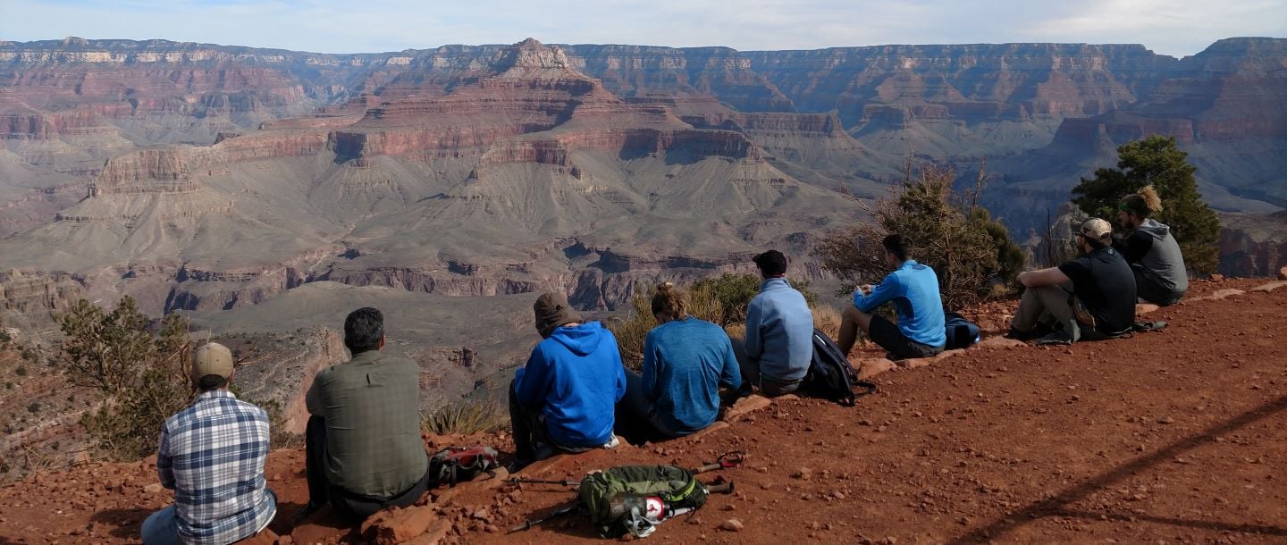 students sitting on a mountain side looking at the surrounding mountains on a sunny day