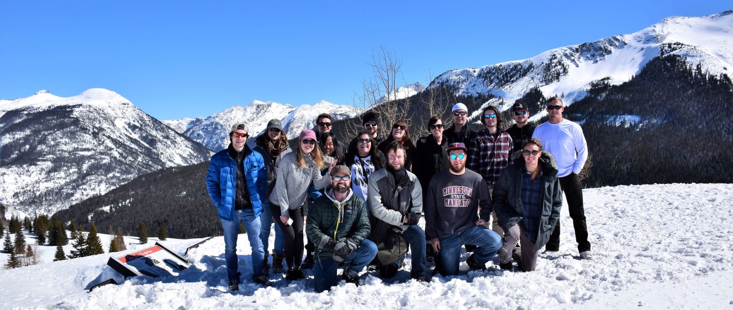 group of students posing outside on a snowy mountain on a sunny day