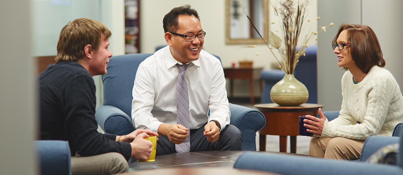 Three people sitting down in a lounge area having a discussion while drinking coffee