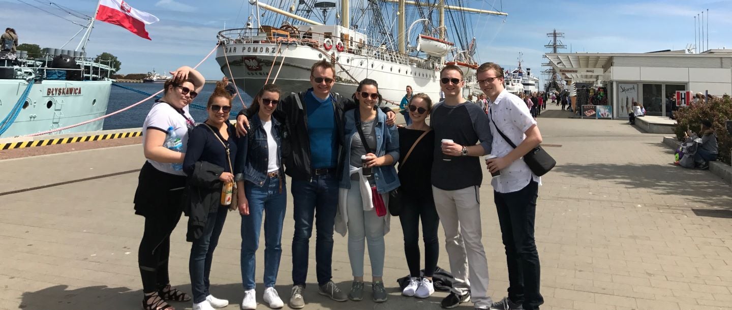 The Political Science students posing on a board walk with ships in the background on their study abroad tour