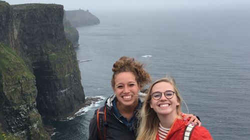Two I-O psychology students posing on a cliff overlooking the ocean while on their international trip