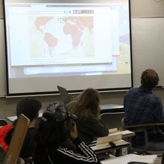 Students sitting in class looking at projections of world maps