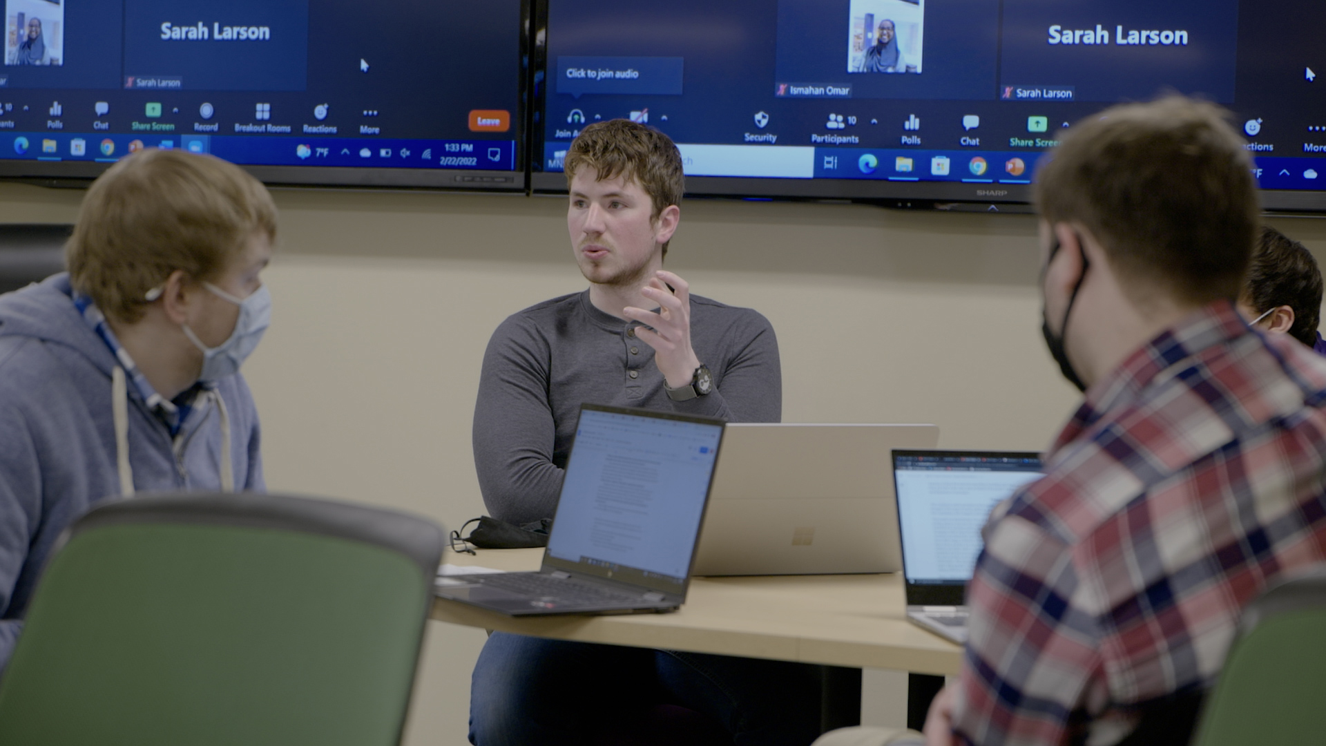 a person sitting at a table with laptops and a group of people