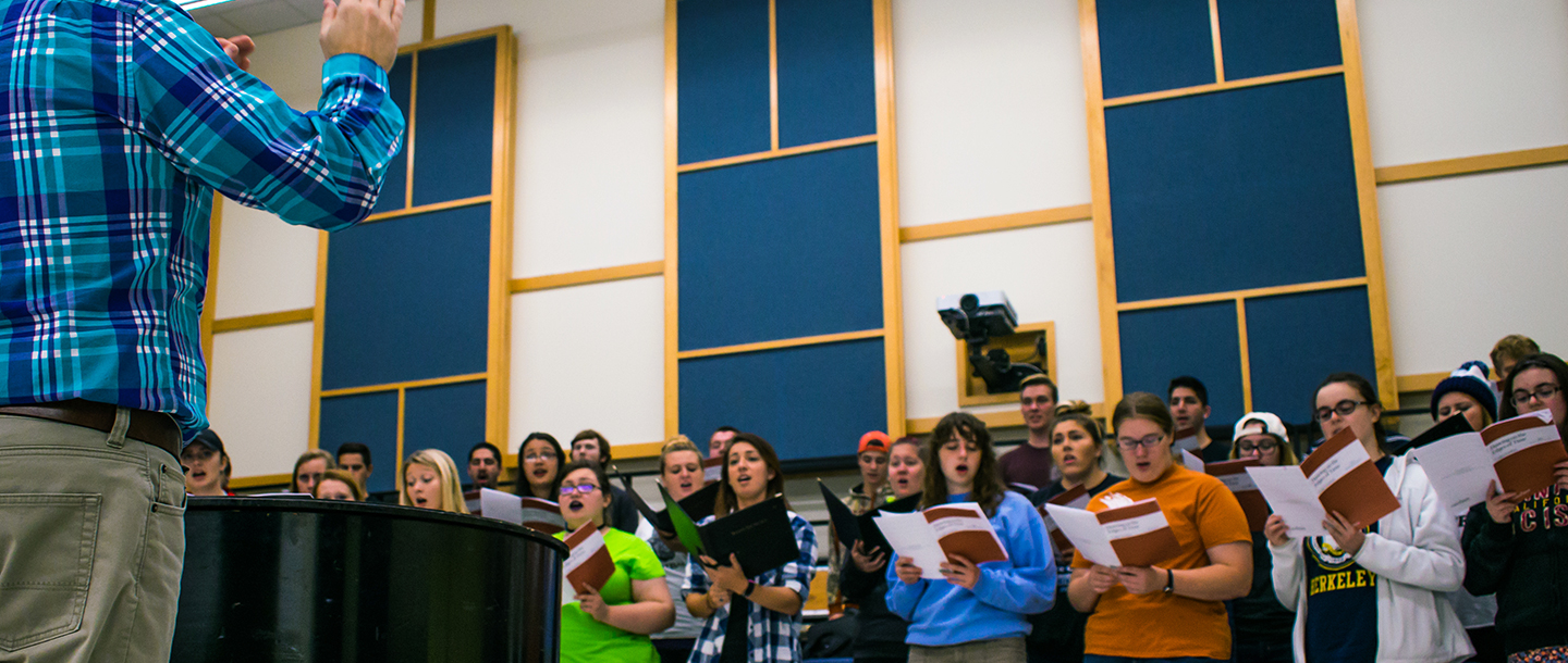 Students of Graduate studies in music signing a song looking at their music book in front of their instructor